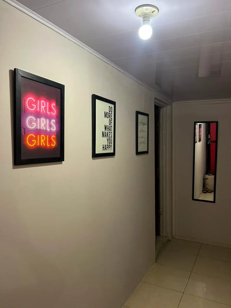 Pasillo del hostel decorado con cuadro de neón 'GIRLS GIRLS GIRLS' y arte motivacional.