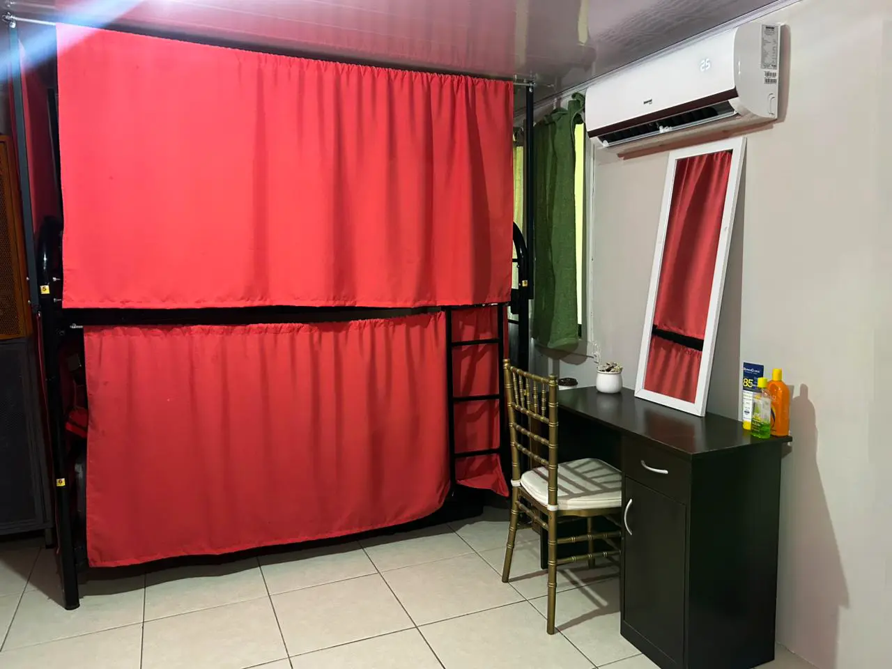Dormitorio femenino con litera, cortinas rojas de privacidad, escritorio y aire acondicionado.