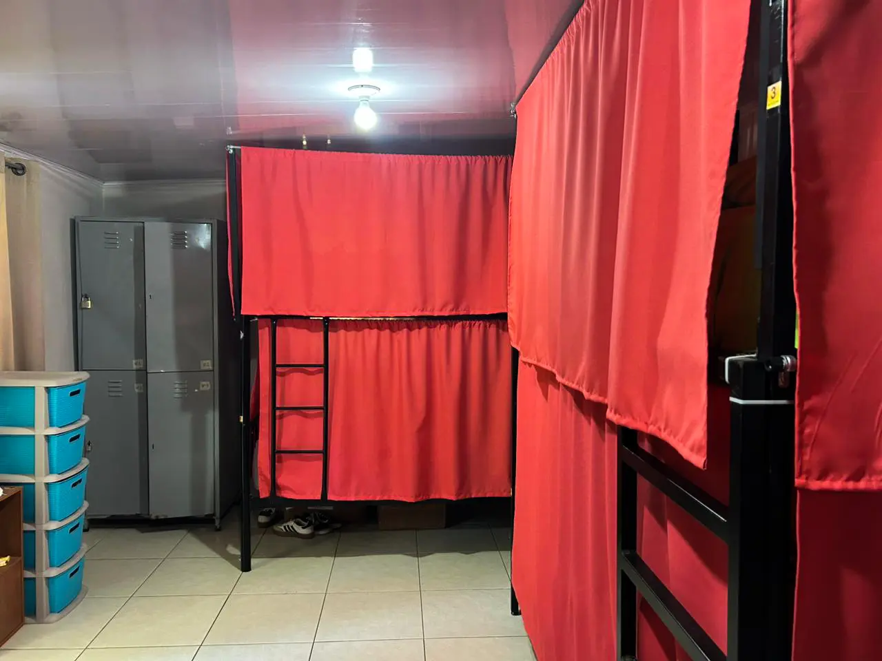 Dormitorio compartido con literas con cortinas y lockers de seguridad al fondo.